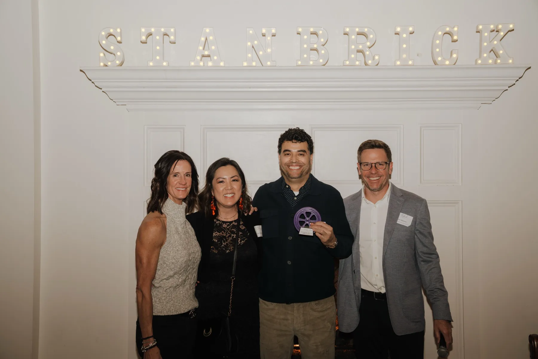 A teammate holding an award beside leadership at the holiday party